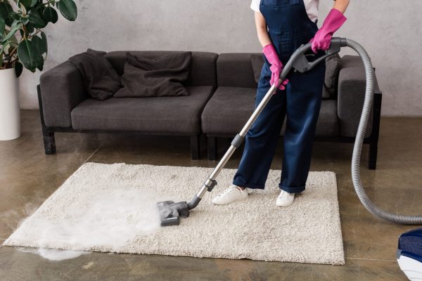 Cropped view of cleaner in overalls and rubber gloves using vacuum cleaner with hot steam on carpet Cropped view of cleaner in overalls and rubber gloves using vacuum cleaner with hot steam on carpet